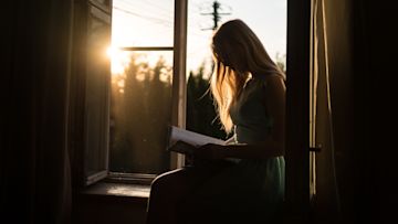 A woman reads a book by a window.