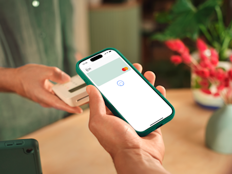 Une personne utilise un smartphone affichant une carte N26 à l'écran pour payer sur un terminal blanc.