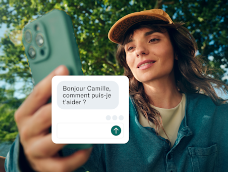 Une femme tient son téléphone vers l'appareil photo, avec une boîte de discussion de service client superposée à l'écran.