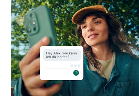 Eine Frau hält ihr Telefon in Richtung Kamera, wobei ein Kundenservice-Chatfenster über den Bildschirm gelegt ist.