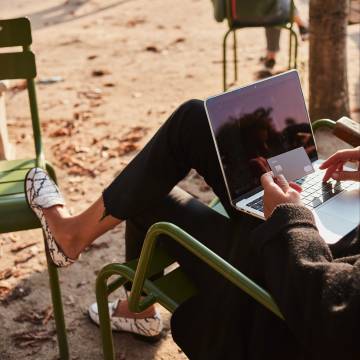 Une femme assise dans un parc de Paris avec son ordinateur portable tenant une carte N26 metal.