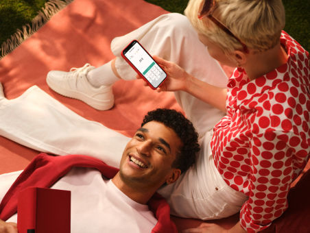 A couple lies on a blanket, with the girl looking at her mobile and the man resting his head on her leg.
