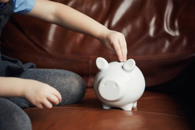 niño que pone una moneda en una hucha.