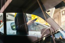 man standing up near a car and checking his smartphone.