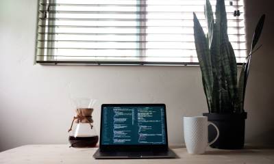 Tisch eines Freelancers mit einem Laptop, Kaffeetasse und einer Pflanze.