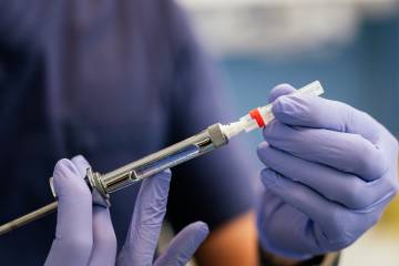 A person wearing rubber gloves holding a syringe.