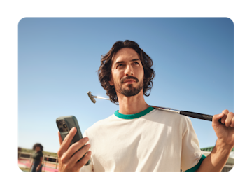 A man holds a smartphone and a golf club over his shoulder while looking up at the sky.