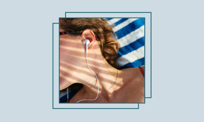 Girl with headphones lying on a striped towel at the beach.