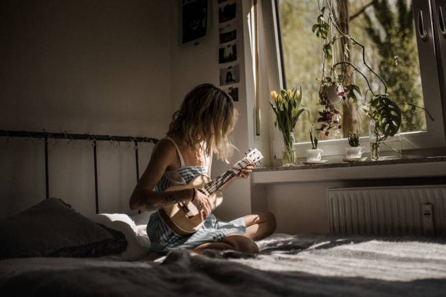 Woman plays an instrument on her bed.