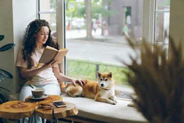 A woman in a coffee shop reading by her dog.