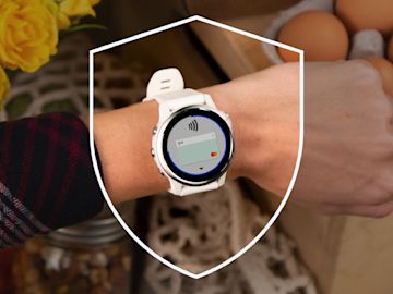 Eine Nahaufnahme des Handgelenks einer Person mit einer weißen Garmin-Smartwatch, die einen kontaktlosen Zahlungsbildschirm anzeigt, mit einer Sicherheits-Schild-Grafik darüber.
