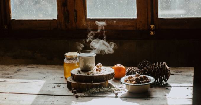 Pine cones, orange, honey, and tea on a table.