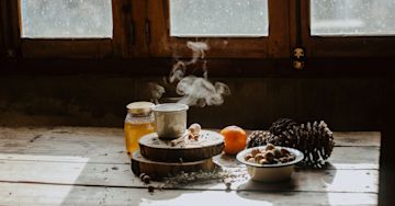 Pine cones, orange, honey, and tea on a table.