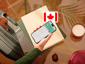 image of a person holding a phone showing an N26 card in the app screen and grabbing a suitcase with the other hand and with a Canadian flag.