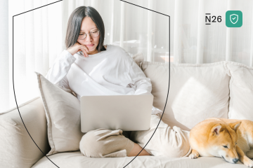 Woman on her laptop with dog on sofa.