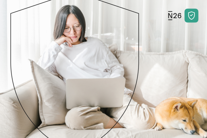 Una mujer en su computadora portátil con un perro en el sofá.