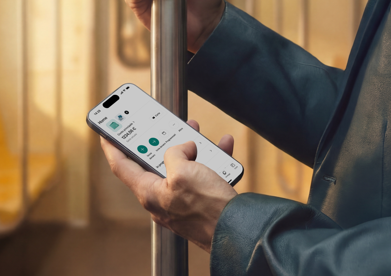 Una persona si tiene a un palo di sostegno su un treno mentre usa uno smartphone che mostra l'interfaccia di un'applicazione di mobile banking.