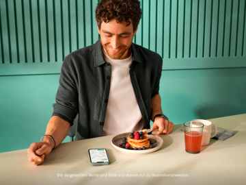 Person, die Pfannkuchen mit Erdbeersaft zum Frühstück isst und sich die Crypto N26-App ansieht.