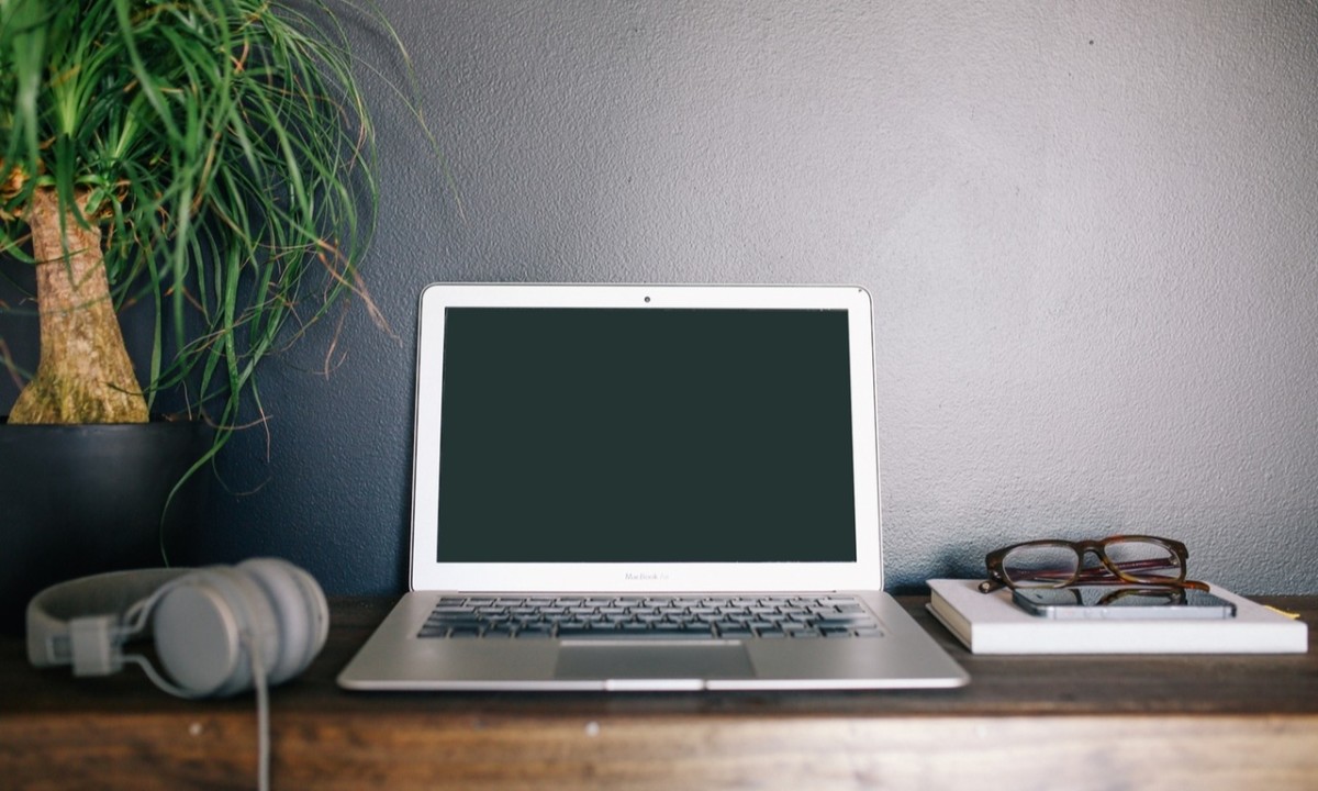 Portatil de un freelance en un escritorio, con gafas y auriculares.