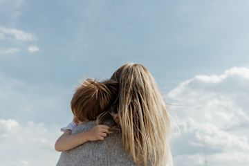 A woman holding a child and looking at the blue sky.