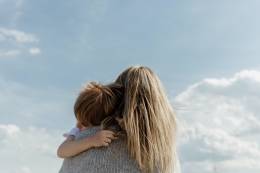 Una donna che tiene in braccio un bambino e guarda il cielo azzurro.