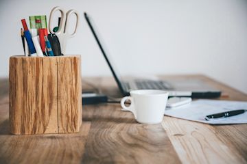 Una tazzina, un portapenne e un laptop appoggiati su una scrivania.