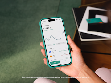 A hand holds a smartphone displaying a cryptocurrency portfolio with a line graph and balances.