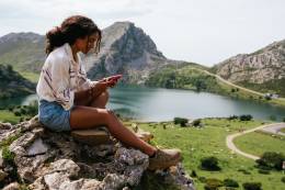 Traveller sitting on the top of a hill and texting about her adventures.