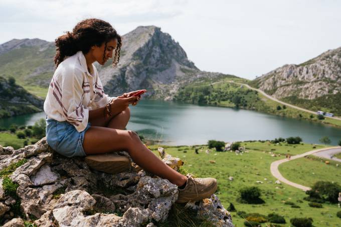 Reisende sitzt auf einem Stein mit Aussicht auf ein Tal mit einem See.