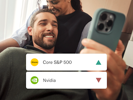 Una pareja sonriente mira un smartphone, con tarjetas superpuestas que muestran los nombres de acciones Core S&P 500 y Nvidia.
