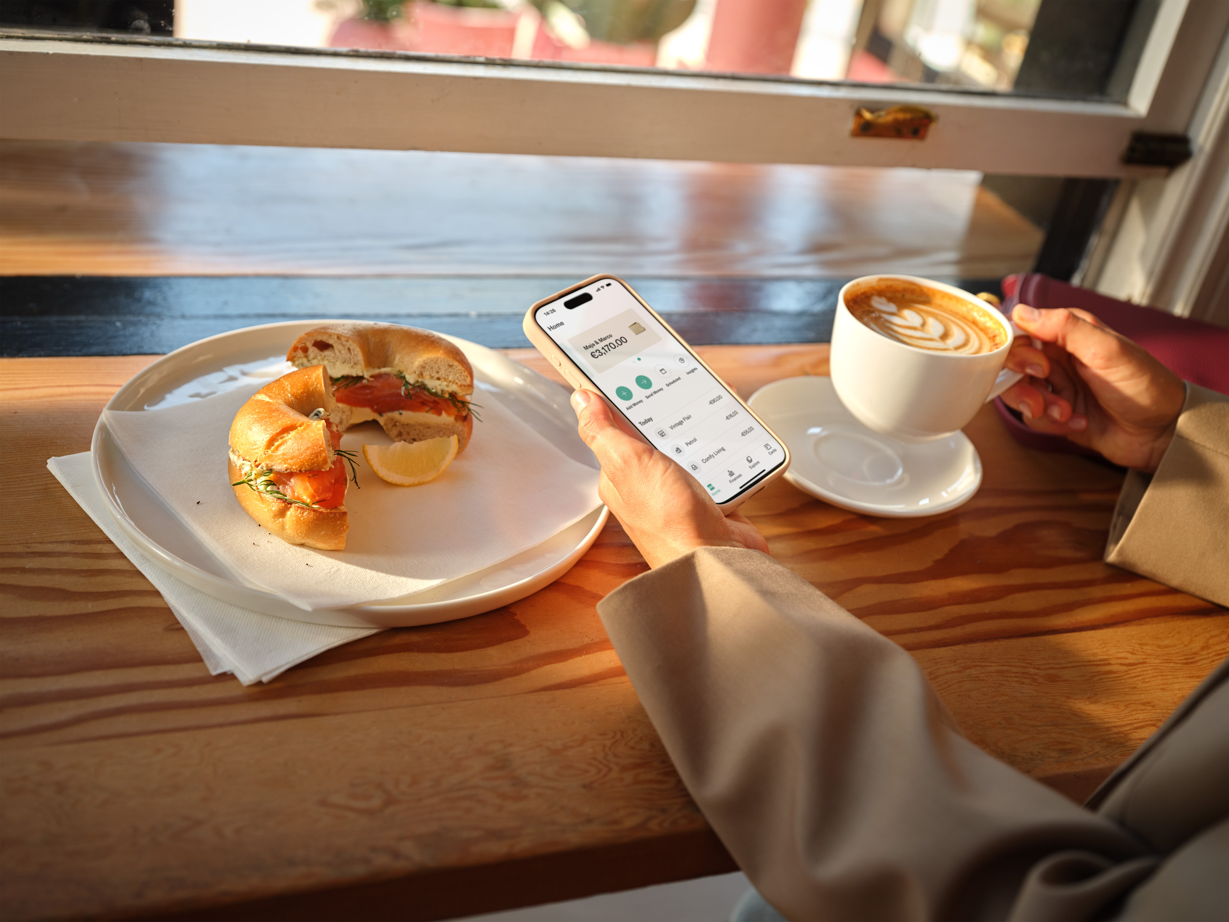 Una persona con il cellulare che controlla il saldo bancario e fa colazione.