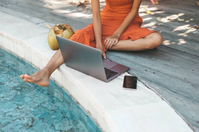 Woman sitting by pool with phone and computer.