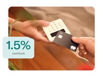 A black N26 Mastercard is being used to make a contactless payment on a white card reader, with "1.5% cashback" written in green on a white rectangle in the bottom left corner.