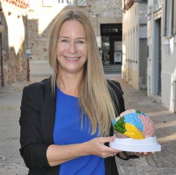 Prof. Dr. Mira Fauth-Bühler sosteniendo el modelo de un cerebro de plástico.