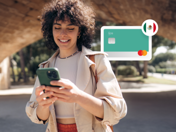 image of a young woman standing up in a park and looking at his phne, with an n26 card and a Mexican flag in the background.