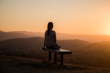 Woman sitting on a bench at sunset.