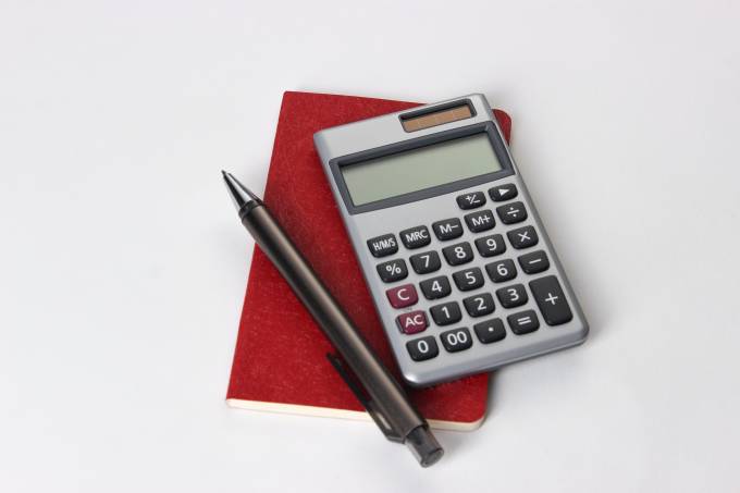 Calcolatrice, penna e quaderno su sfondo bianco.