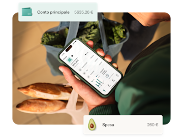 Una mano tiene uno smartphone che mostra l'app bancaria N26 con carte sovrapposte per il conto principale e un budget per la spesa.