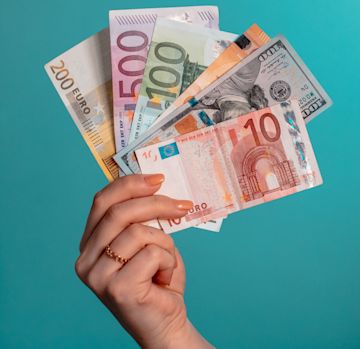 Una mano ofreciendo una donación con billetes de diferentes paises.