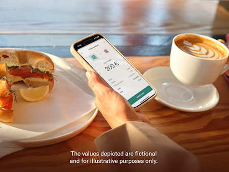 A hand holds a smartphone displaying the N26 order preview screen for a stock investment at a cafe table.