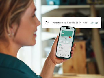Une femme regarde l'écran de son smartphone qui affiche l'interface de l'application N26 pour configurer des portefeuilles mobiles et en ligne.