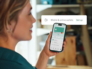 A woman looks at her smartphone screen which displays the N26 app interface for setting up mobile and online wallets.