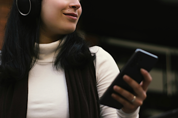 A woman listening to music looks at her phone while planning her new year's finances. 