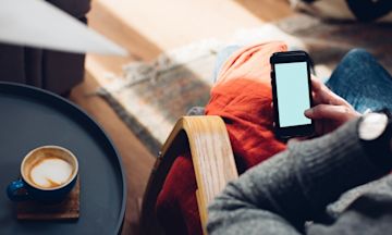 Un uomo è seduto su una sedia, beve caffè e controlla il suo telefono come aprire un conto in banca.
