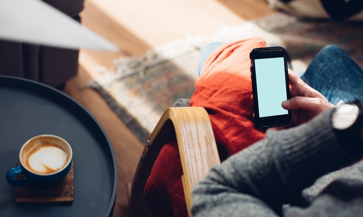 Un hombre está sentado en una silla, tomando café y comprobando en su teléfono cómo abrir una cuenta bancaria.