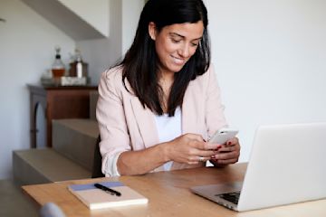 Frau am Schreibtisch mit Handy und Computer.