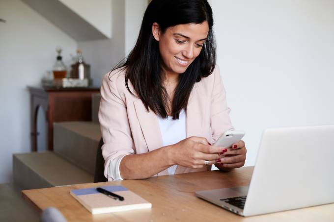 Une femme avec un smartphone et un ordinateur portable assise à un bureau.