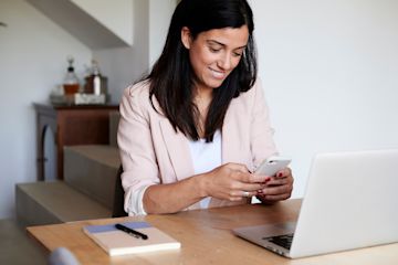 Une femme avec un smartphone et un ordinateur portable assise à un bureau.