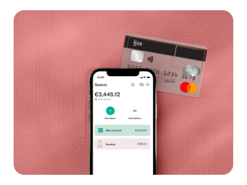 The N26 app displays the balance in Spaces, accompanied by a transparent N26 card against a rhubarb-colored background.