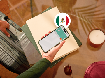 image of a person holding a phone showing an N26 card in the app screen and grabbing a suitcase with the other hand and with a Mexican flag.